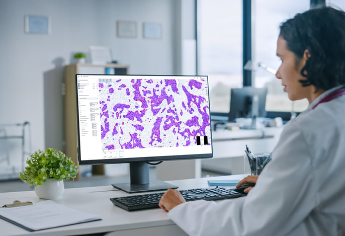 Healthcare professional looking at monitor featuring digitized tissue sample image.